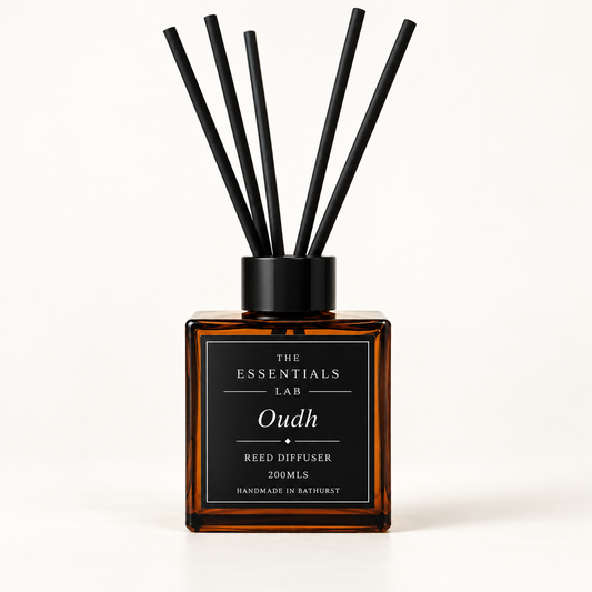 A reed diffuser bottle by The Essentials Lab in amber glass with a black cap and six black reeds, featuring a black label with white text on a clean white background.