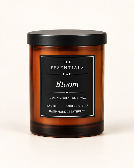 An amber glass jar candle with a black lid and a black label reading 'THE ESSENTIALS LAB Bloom' on a clean white background.